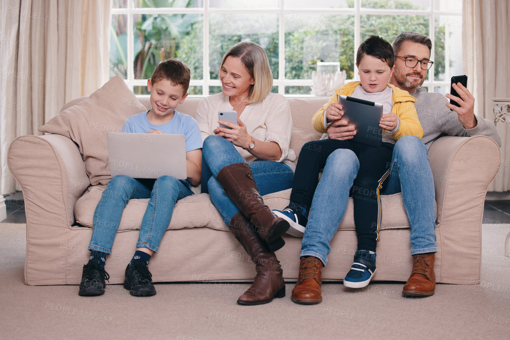 Buy stock photo Shot of a young family bonding while using their electronic devices together at home