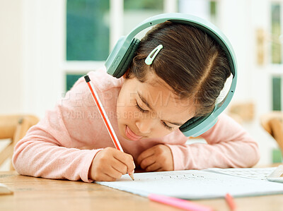 Buy stock photo Cropped shot of an adorable little girl listening to music while doing her homework