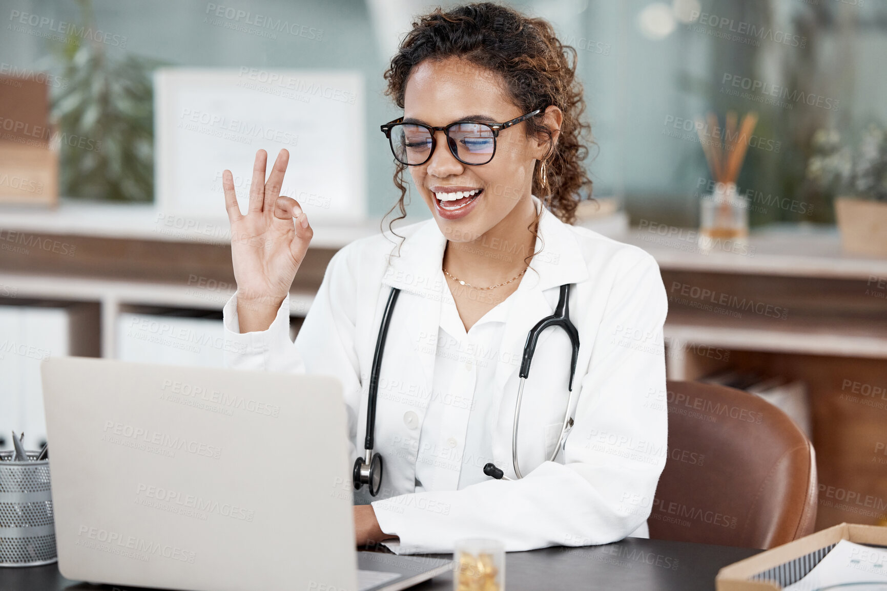 Buy stock photo Female doctor, laptop and video call with okay, smile and office for remote consultation. Woman, conference and virtual examination with telehealth or appointment schedule with positivity in Germany.