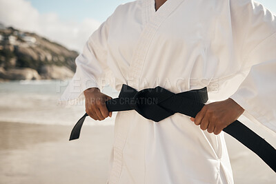 Buy stock photo Cropped shot of an unrecognizable female martial artist tying her black belt while practicing karate on the beach