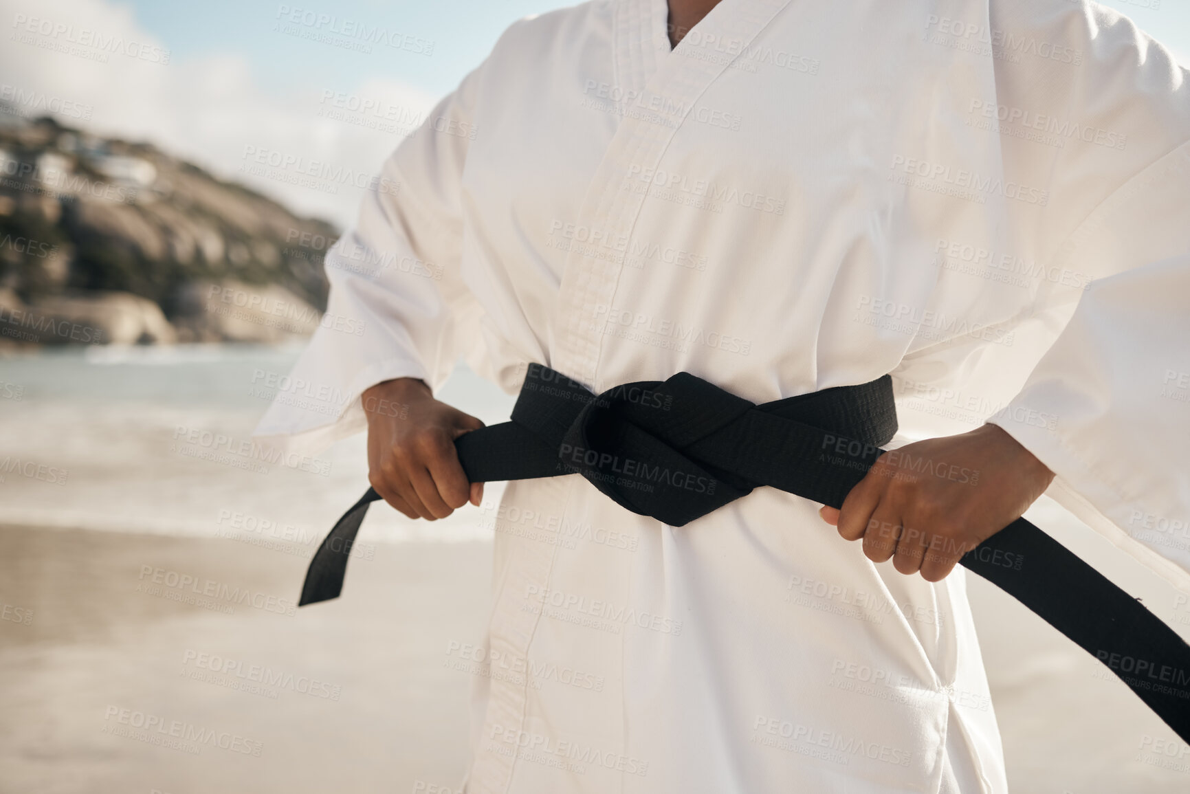 Buy stock photo Cropped shot of an unrecognizable female martial artist tying her black belt while practicing karate on the beach