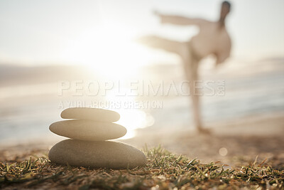 Buy stock photo Closeup shot of a stack of stones on the beach with a man practicing karate in the background