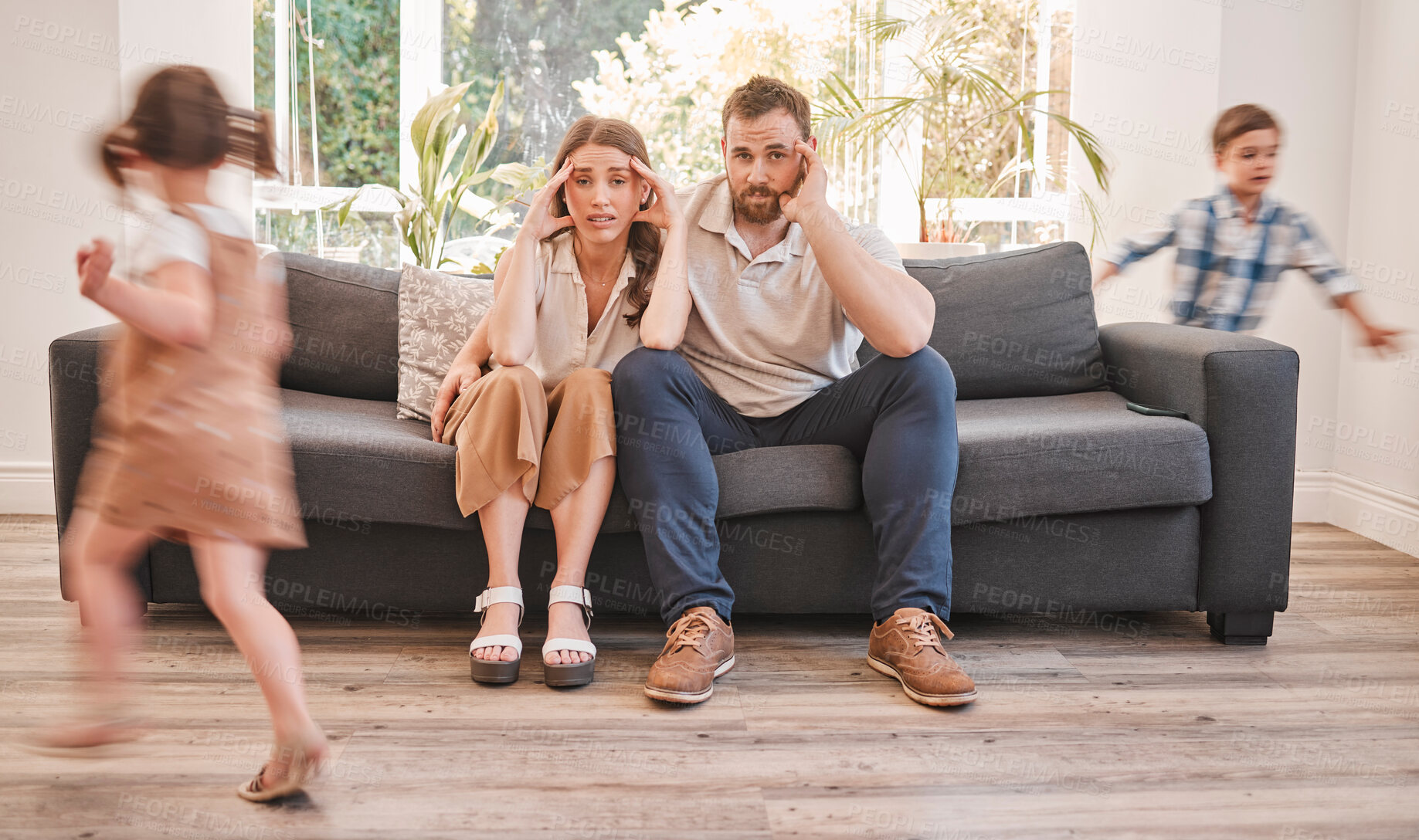 Buy stock photo ADHD kids, headache and parents on sofa with stress, overwhelmed and hyper active energy at home. Mom, dad and children running at couch with bad behavior, noise and chaos with motion blur in lounge