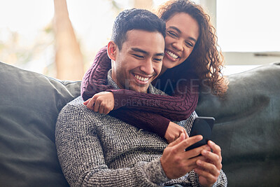 Buy stock photo Happy couple, phone and sofa laughing for social media, internet meme or online streaming service at home. Young interracial woman and man or partner on website, connection and hug or love on couch