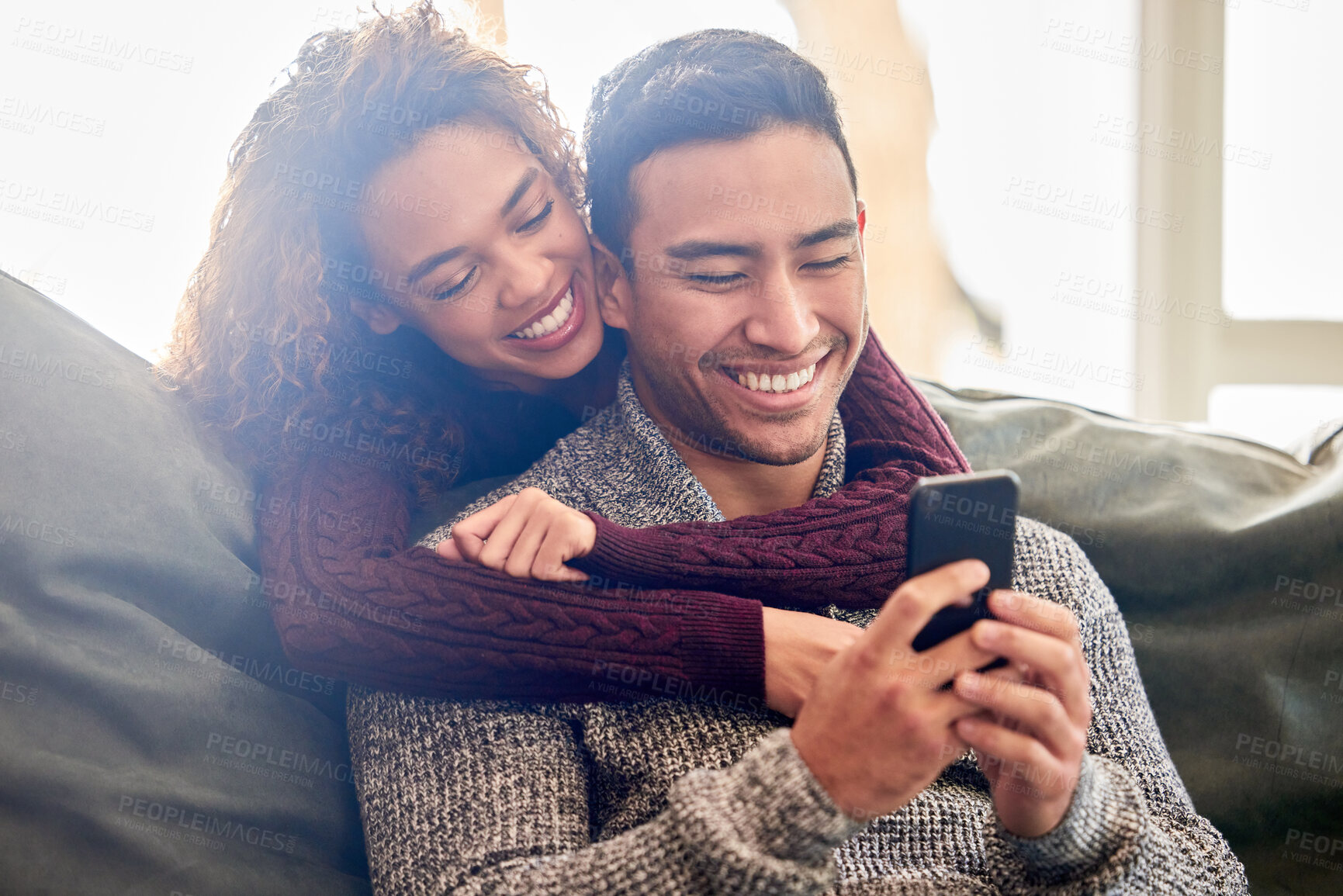 Buy stock photo Happy couple, phone and hug on couch with internet meme, reading news or online streaming service at home. Young interracial woman and man or partner on funny website, connection and love on sofa