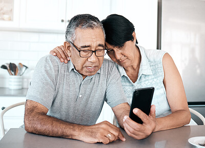 Buy stock photo Shot of a senior couple looking unhappy while using a phone at home