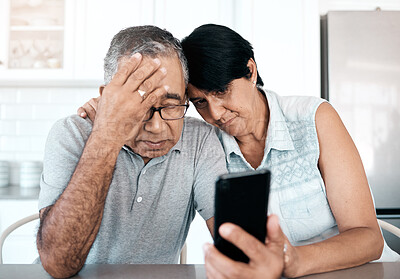 Buy stock photo Shot of a senior couple looking unhappy while using a phone at home