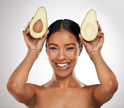 Buy stock photo Studio portrait of an attractive young woman posing with two halves of an avocado against a grey background