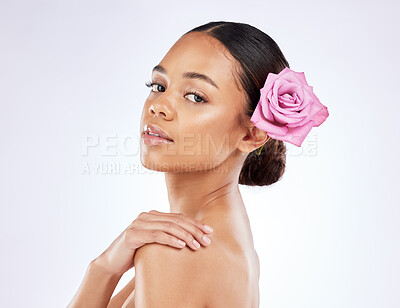 Buy stock photo Shot of a beautiful young woman posing with a rose tucked behind her ear against a studio background