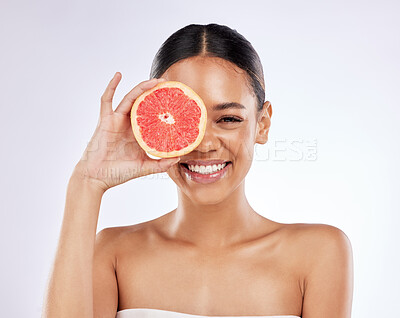 Buy stock photo Shot of a beautiful young woman covering her eye with a grapefruit against a studio background