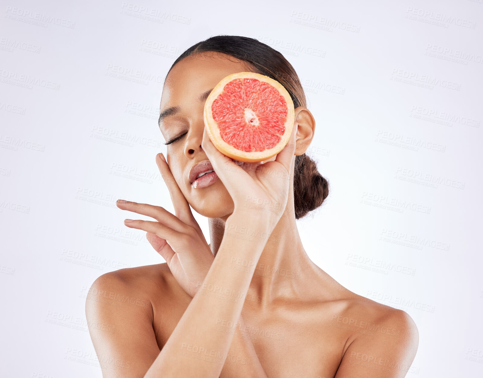 Buy stock photo Shot of a young woman posing with cut grapefruit against a studio background