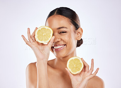 Buy stock photo Shot of a beautiful young woman covering her eye with a lemon against a studio background