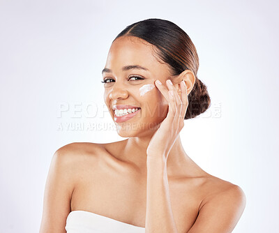 Buy stock photo Shot of a young woman applying moisturiser to her face against a studio background