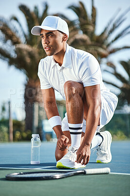 Buy stock photo Full length shot of a handsome young man kneeling down to tie his shoelaces before tennis practice