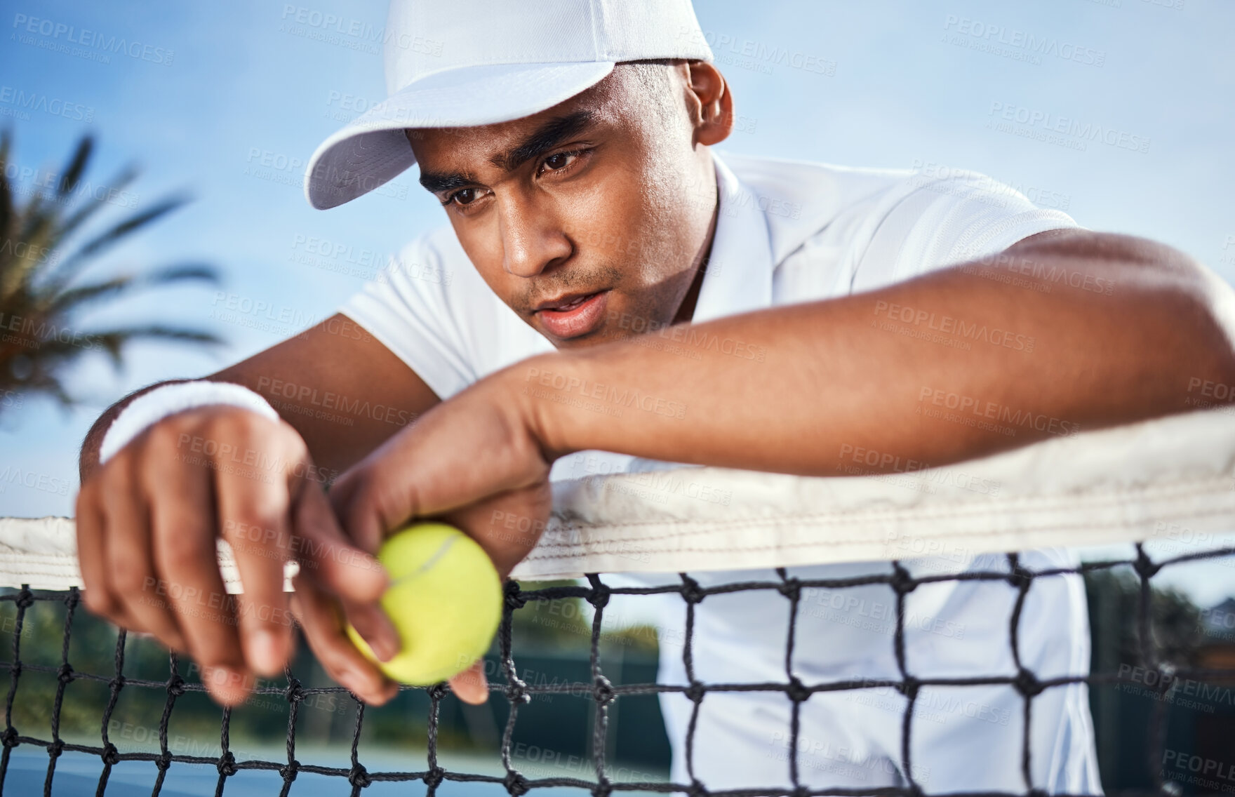 Buy stock photo Shot of a handsome young man leaning on a tennis net and looking disappointed after practice