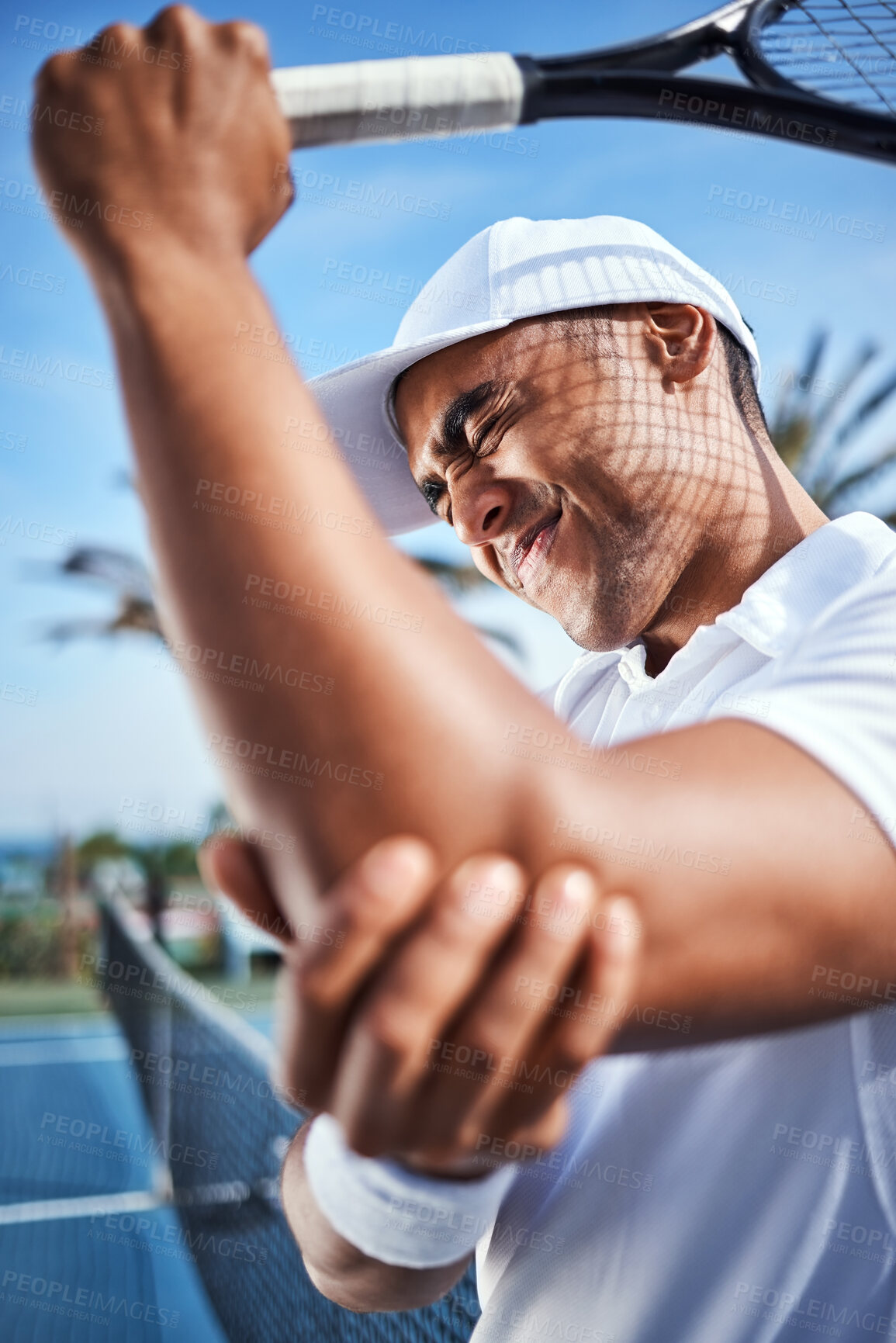 Buy stock photo Shot of a handsome young man standing alone and suffering from an elbow injury during a game of tennis