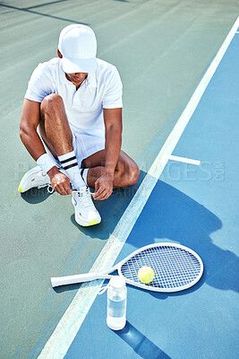 Buy stock photo Full length shot of an unrecognisable man sitting alone and tying his shoelaces before tennis practice