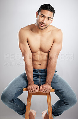 Buy stock photo Studio shot of a handsome young man showing off his muscular body while sitting on a chair against a grey background