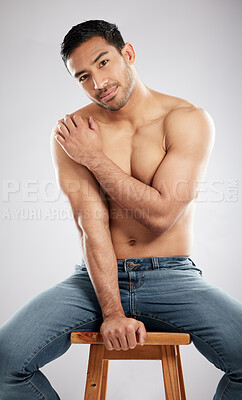 Buy stock photo Studio shot of a handsome young man showing off his muscular body while sitting on a chair against a grey background