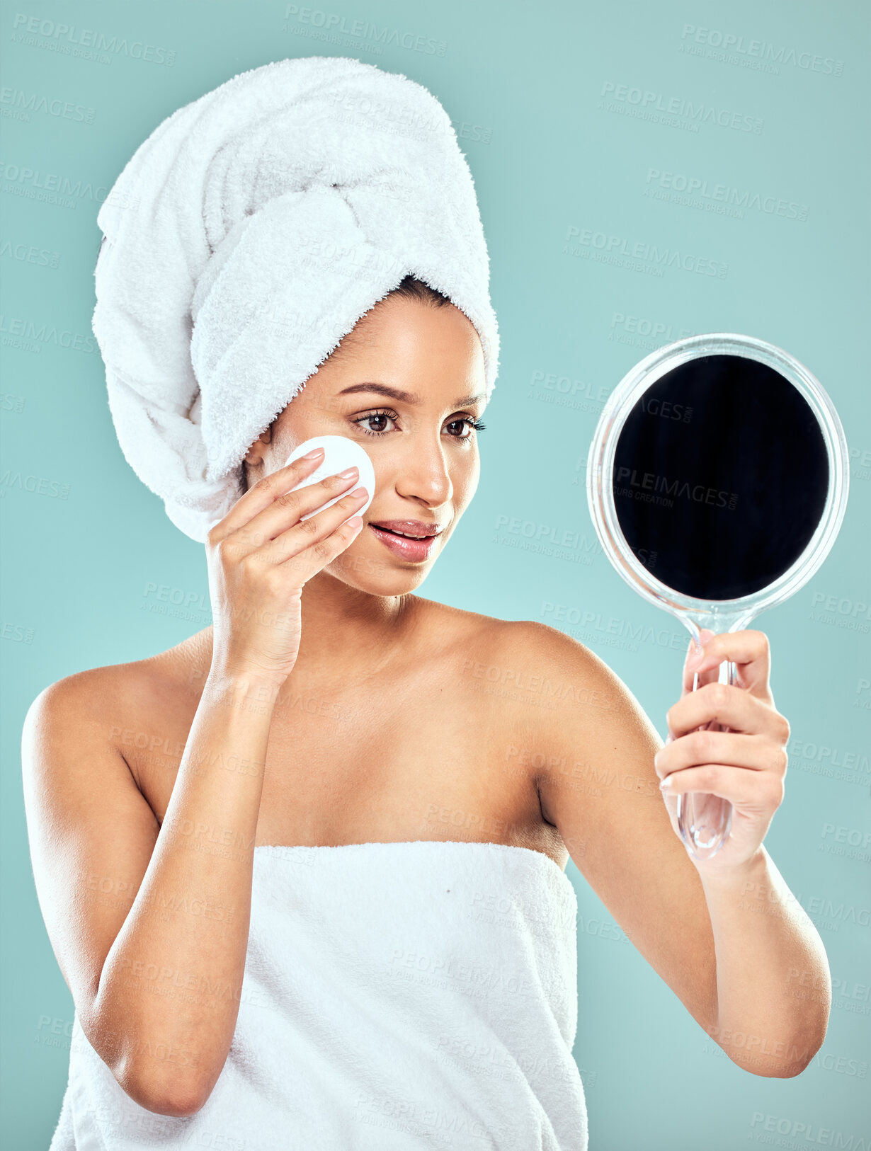 Buy stock photo Shot of a young woman applying product to her face with a cotton pad while looking in a mirror against a studio background