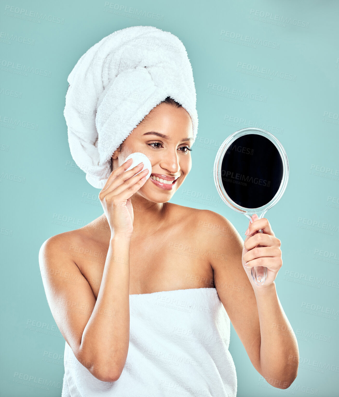 Buy stock photo Shot of a young woman applying product to her face with a cotton pad while looking in a mirror against a studio background