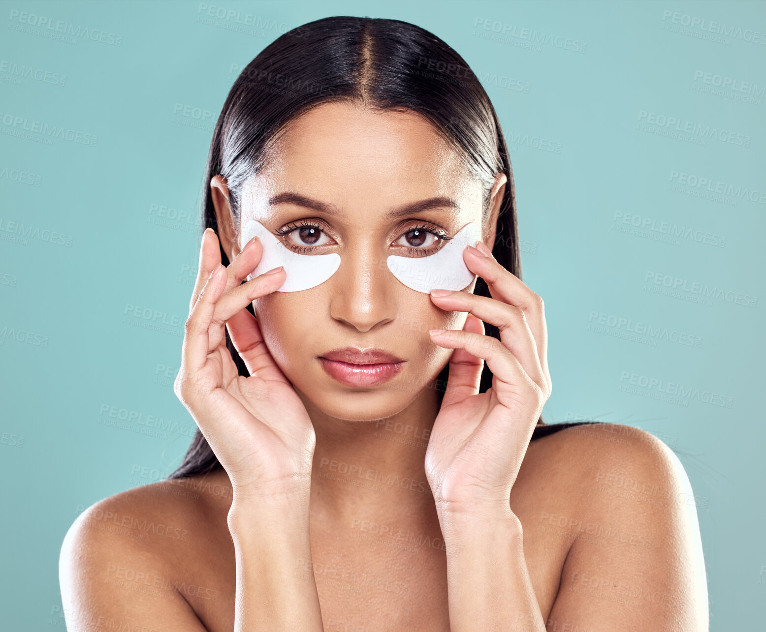 Buy stock photo Shot of a young woman using eye masks against a studio background