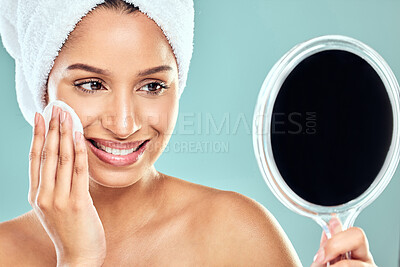 Buy stock photo Shot of a young woman applying product to her face with a cotton pad while looking in a mirror against a studio background