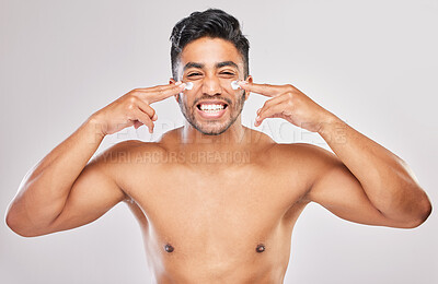 Buy stock photo Shot of a young man applying lotion to his face against a grey background