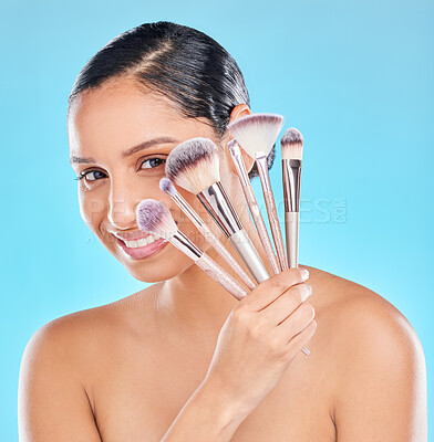 Buy stock photo Studio portrait of an attractive young woman posing with a bunch of makeup brushes against a blue background