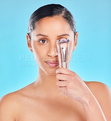 Buy stock photo Studio portrait of an attractive young woman posing with a bunch of makeup brushes against a blue background