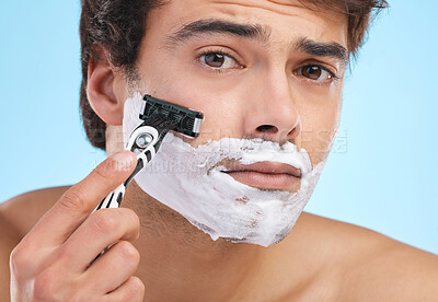 Buy stock photo Portrait, razor and man shaving with cream for skincare, hygiene or grooming isolated on blue background in studio. Foam, face and model cut beard for hair removal, beauty and cleaning for wellness