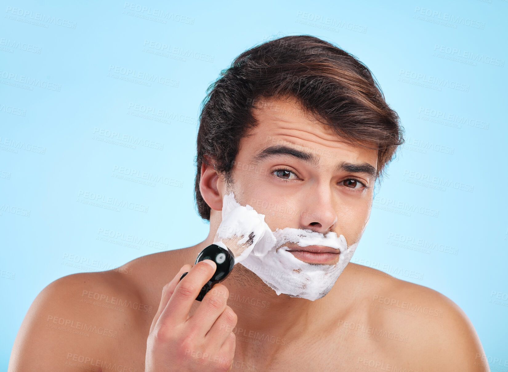 Buy stock photo Portrait, man and shaving cream brush in studio for hair removal, hygiene and grooming isolated on blue background. Face, beard and model apply foam for skincare, beauty and cleaning for wellness