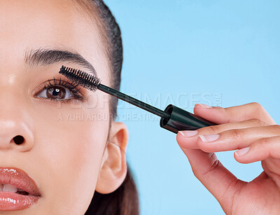 Buy stock photo Studio portrait of an attractive young woman applying mascara against a blue background