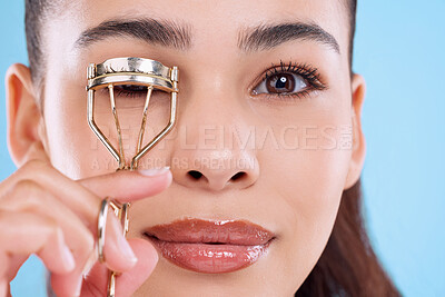 Buy stock photo Studio portrait of an attractive young woman using an eyelash curler against a blue background