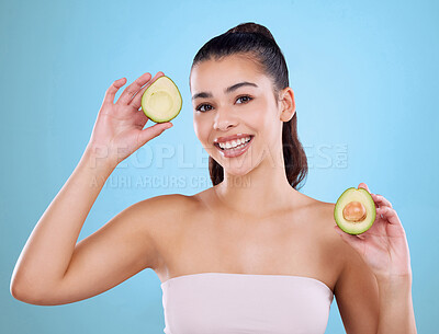 Buy stock photo Studio portrait of an attractive young woman posing with two halves of an avo against a blue background