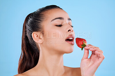 Buy stock photo Studio shot of an attractive young woman biting into a strawberry against a blue background