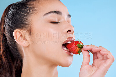Buy stock photo Studio shot of an attractive young woman biting into a strawberry against a blue background