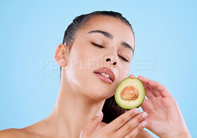 Buy stock photo Studio shot of an attractive young woman posing with half an avo against a blue background