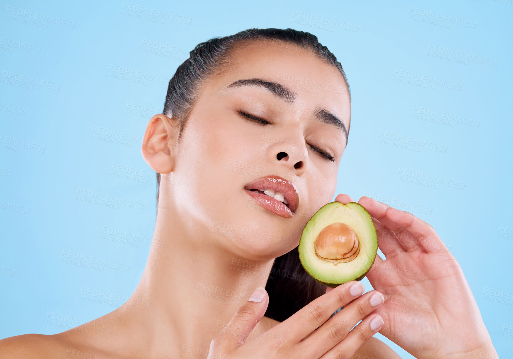 Buy stock photo Studio shot of an attractive young woman posing with half an avo against a blue background
