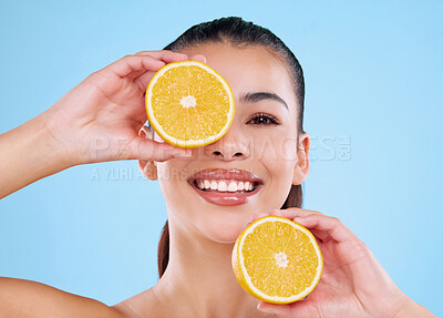 Buy stock photo Studio portrait of an attractive young woman posing with two halves of an orange against a blue background