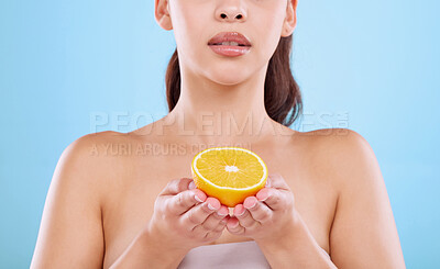 Buy stock photo Studio shot of an unrecognizable young woman posing with half an orange against a blue background