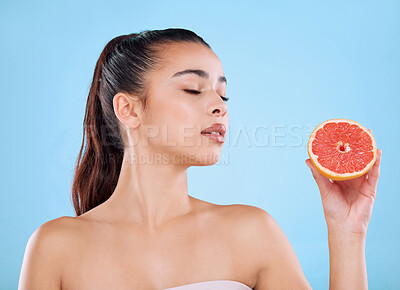 Buy stock photo Studio shot of an attractive young woman posing with half a grapefruit against a blue background