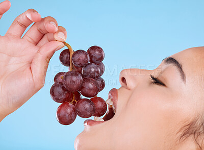 Buy stock photo Studio shot of an attractive young woman biting into a bunch of grapes against a blue background