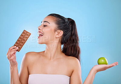 Buy stock photo Studio shot an attractive young woman deciding between a chocolate and an apple against a blue background