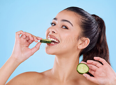 Buy stock photo Studio portrait of an attractive young woman biting into a slice of cucumber against a blue background