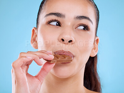 Buy stock photo Studio shot of an attractive young woman biting into slab of chocolate against a blue background