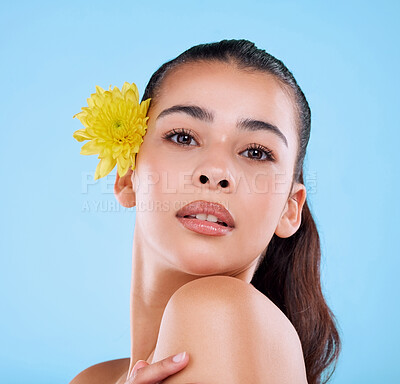 Buy stock photo Studio portrait of an attractive young woman posing with a flower behind her ear against a blue background