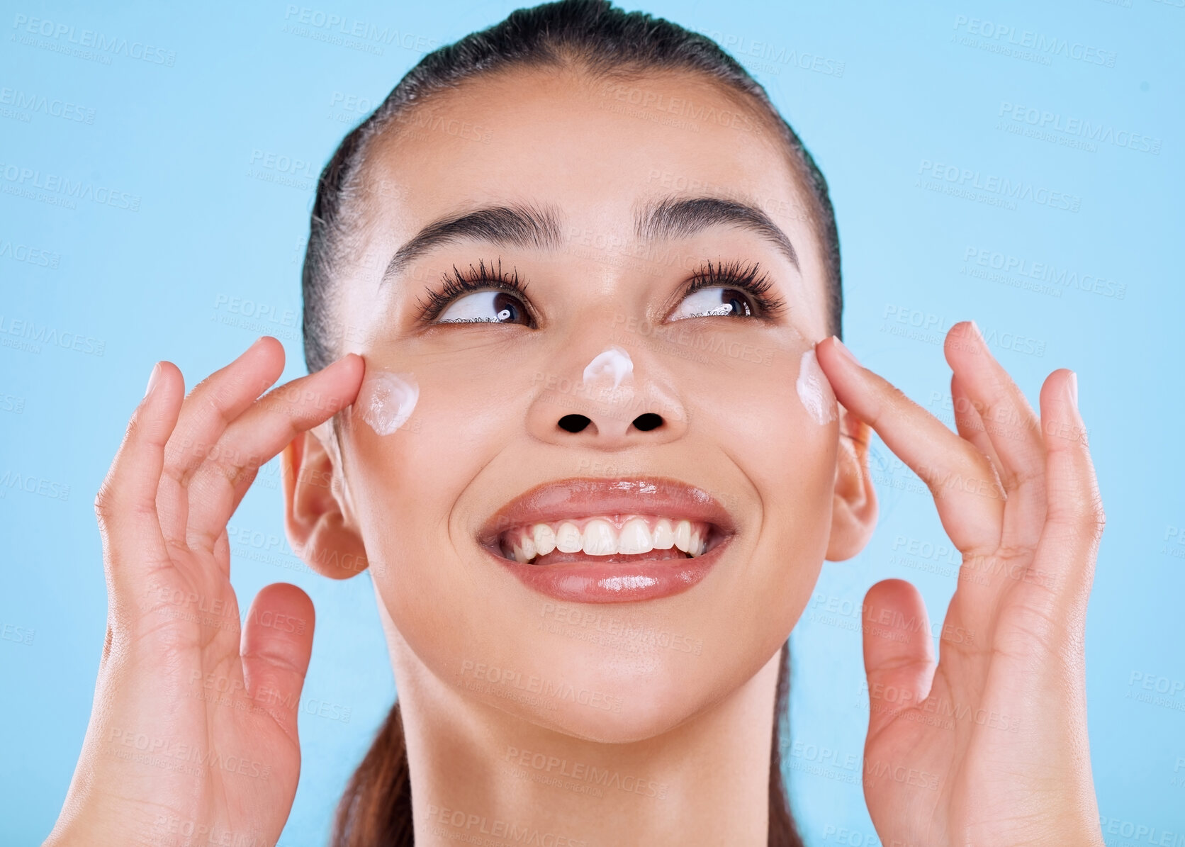 Buy stock photo Studio shot of an attractive young woman applying moisturizer against a blue background