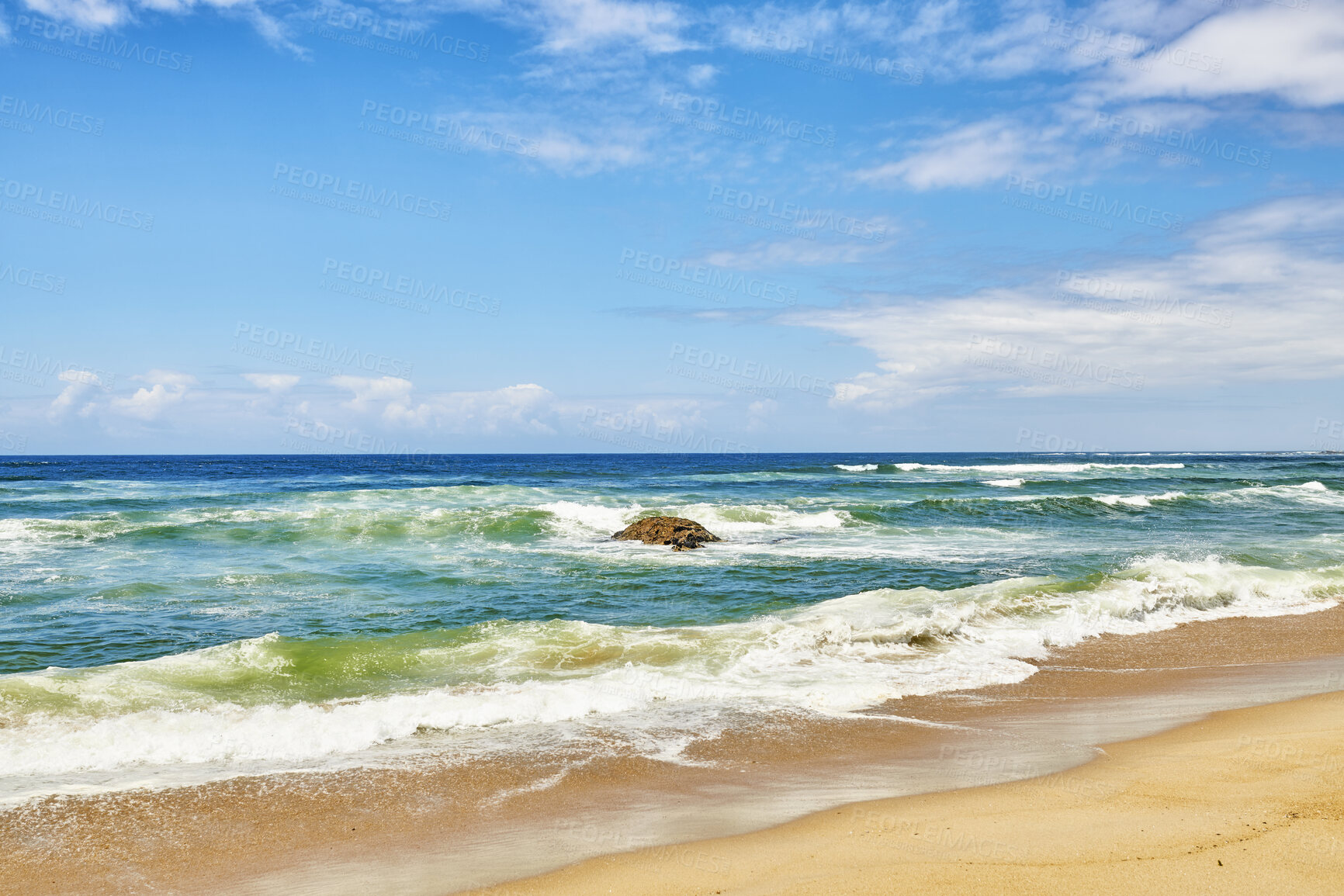 Buy stock photo Ocean waves, turbulent sea and rough tides from strong winds crashing onto a boulder at the beach shore with a cloudy blue sky copy space background. Rocky seaside view, landscape and coastal scenery