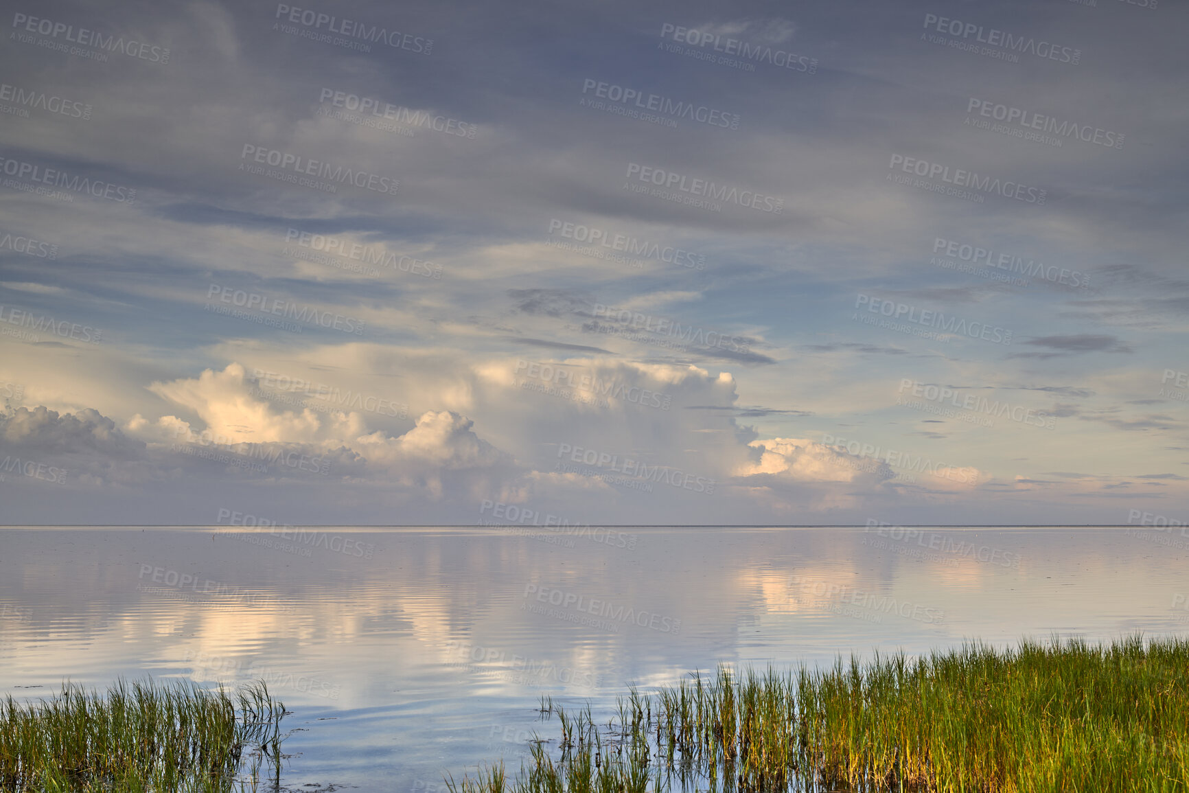 Buy stock photo A beautiful calm and quiet view of lake water with a cloudy sky reflection and green grass on the bank. The landscape of a magical horizon with copy space outdoors in nature or a peaceful environment